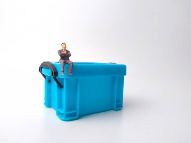 Minyatür insanlar beyaz arka planda mavi bir minyatür kutunun üzerinde oturuyorlar.