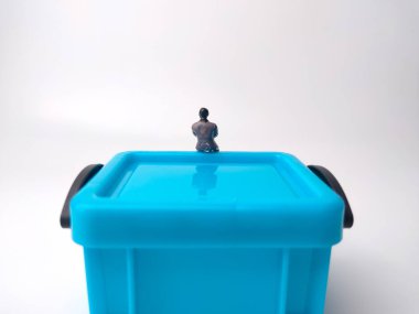 Minyatür insanlar beyaz arka planda mavi bir minyatür kutunun üzerinde oturuyorlar.