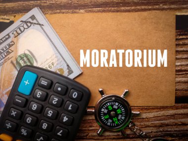 Tahta zemin üzerinde Moratorium metin ile üst görünüm hesap makinesi, pusula ve banknotlar.