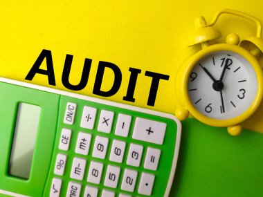 Yeşil ve sarı arkaplanda AUDIT metni bulunan üst görünüm saati ve hesap makinesi.