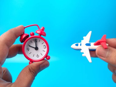 Mavi arka planda el ele tutuşan saat ve oyuncak uçak. Seyahat konsepti.