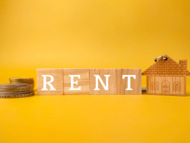 Ev anahtarlığı, bozuk paralar ve sarı arka planda kelime RENT olan tahta küp..