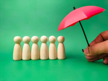 Tahta bebek, plan, aileyi kurtarmak, risk ve krizi önlemek, sağlık ve sigorta kavramını korumak için tahta bebek düzeniyle el ele tutuşan kırmızı şemsiye..