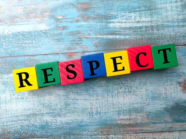 Colored wooden cube with word RESPECT on a blue wooden background.