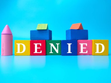 Colored wooden cube with word DENIED on a blue background. clipart