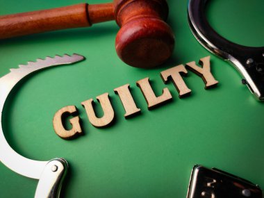 Metal kelepçe ve ahşap tokmak ile yeşil arka planda GUILTY metni.
