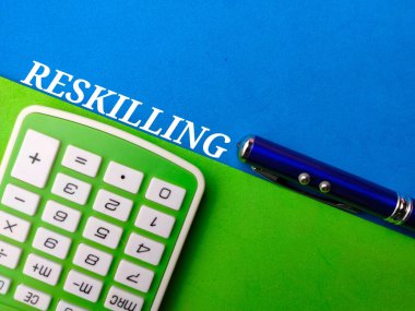 Mavi ve yeşil arka planda RESKILLING sözcüğüne sahip hesap makinesi ve kalem. İş konsepti.