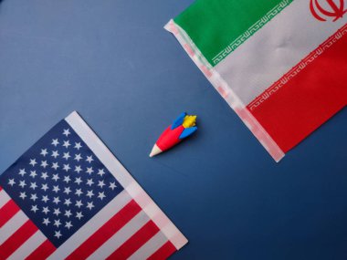 Mavi arka planda Amerika ve İran bayrağı arasında bir roket. Jeopolitik kavram.