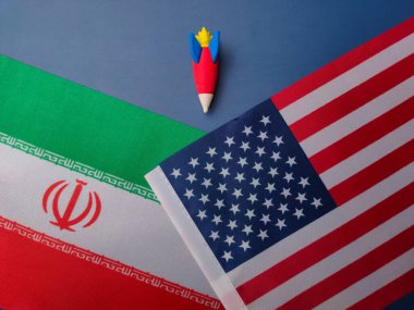 Mavi arka planda Amerika ve İran bayrağı arasında bir roket var. Jeopolitik kavram..
