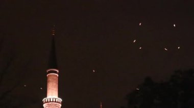 Gece kuş göçü. Kuşlar yanan minarenin etrafında dönüyor. Gökyüzünde uçan kuş sürüsü. Kuşbilim