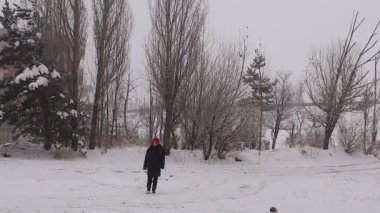 Sıcak giyimli genç kız öğrenci, kısmen karla kaplı bir sabahta Erzurum, Türkiye 'de kısmen karla kaplı ağaçlarla karda yürüyor, okula gidiyor ve kışın dondurucu güzelliğini kucaklıyor.