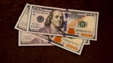 100 dolarlık banknotlar tek tek dökülüp, 1100 dolarlık temiz bir yığın oluşturuyor. Yavaş ve büyüleyici düşüş, paranın zarafetini ve zenginliğin cazibesini ön plana çıkarıyor..