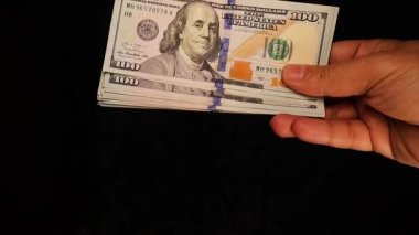 100 dolarlık banknotlarla dolu bir tomar el, kusursuz bir finansal işlemle başka bir ele geçiyor. Temiz ve profesyonel bir ortamda ele geçirilen para, iş ve servet transferinin sembolü..