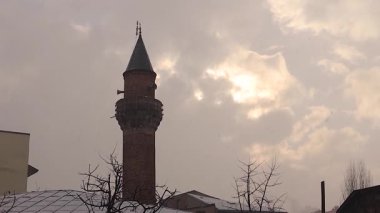 Şiddetli kar yağışı, heybetli bir minarenin dimdik durduğu sahneyi örtüyor. Bunun arkasında, bulutlar yavaşça kayboluyor, Türkiye 'nin Erzurum kentindeki ilk güneş ışınlarını ortaya çıkarıyor, doğanın güzelliği İslami mimariyle buluşuyor.