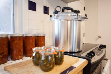 Kavanozlarda Canning biberleri ve düdüklü tencereli chili. Bahçecilik ve çiftçiliğin anahtarı yiyecekleri korumaktır. Basınç konservesi yemek rafını dengede tutar.. 