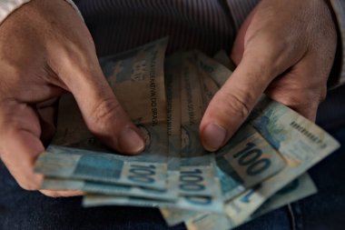 Rio de Janeiro (RJ), Brezilya - 03 / 10 / 2024 - Para Aklama 'nın resimsel resmi ve çamaşır ipinde kurumuş gerçek banknotlar. Bozuk paralar yıkılıyor ve birinin eli yasadışı para sayıyor. 100 real Reais banknotları.