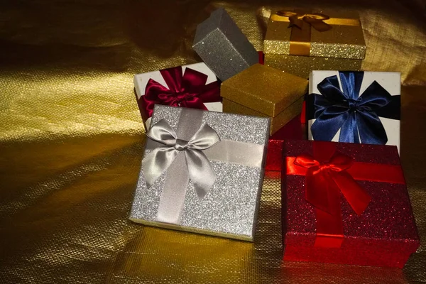 Gift boxes of various colors and with matching bows, on a golden background and with light reflections