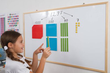 A child learns to count with a white magnetic board in a classroom. clipart