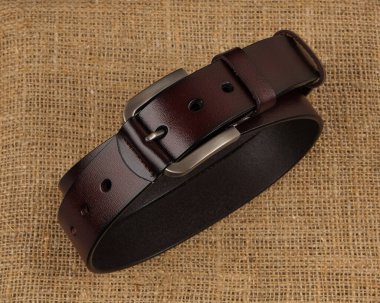 Koyu kırmızı deri kemer, gümüş tokalı, kaba desenli kumaş kumaş üzerine yerleştirilmiş. Moda, yaşam tarzı ya da ürün sergisi projeleri için mükemmel