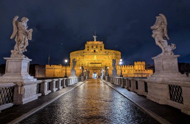 İtalya, Roma 'daki ikonik Castel Sant' Angelo yakınlarındaki St. Angelo Köprüsü 'nün nefes kesici bir akşam sahnesi. Heykeller spot ışıkları altında parlıyor ve büyülü bir atmosfer yaratıyor. Turistler için görülmesi gereken bir yer!