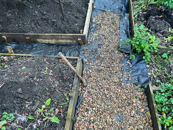 Landscape of building garden project of raised bed paths with wood planking as edging to border organic growing plots, black ground cover sheeting on pathway with gravel to complete the lanes outdoors