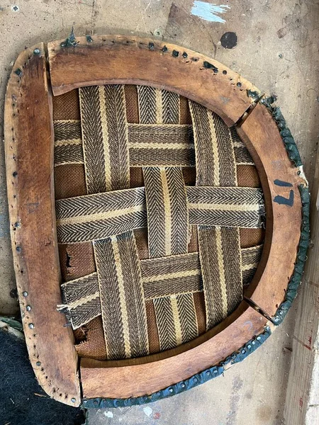 Close up of upholstery on vintage antique chair wood base of broken frame and cotton webbing held with tacks and horse hair stuffing of leather seat cover ready for hand made repair and re-upholstery