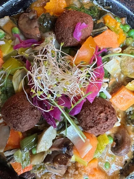 Baharatlı hindistan cevizi soslu taze sebzeli vejetaryen yemeği tatlı patates, havuç, bezelye filizleri, fölafel ile karışık sebzeler ve tereyağlı fasulye filizleri restoran odununun üzerine serpilmişti.