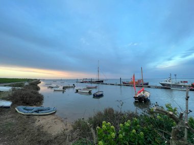 Günbatımının güzel deniz manzarası sakin deniz kıyısı Wells 'te okyanusun ufuk çizgisine yakın Norfolk' ta Doğu Anglia 'da deniz kenarı sakin yüksek sularda demirli tekneler bahar akşamı gökyüzü bulutu olsa da