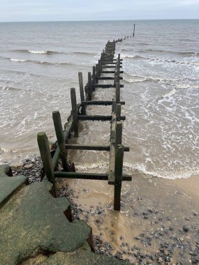 Overstrand Norfolk 'un kumlu ve güzel sahilinin kıyısındaki ahşap dalgakıran. Bulutlu havada okyanus boyunca ufuk boyunca uzanan doğu Anglia manzarası..