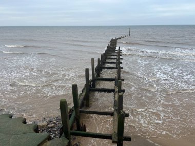 Overstrand Norfolk 'un kumlu ve güzel sahilinin kıyısındaki ahşap dalgakıran. Bulutlu havada okyanus boyunca ufuk boyunca uzanan doğu Anglia manzarası..