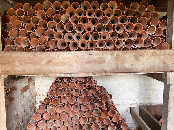 Close up of stack of old clay terracotta clay plant pots on store cupboard shelves for re use planting in brick constructed garden buildings wood shelf potting shed environment country estate Essex