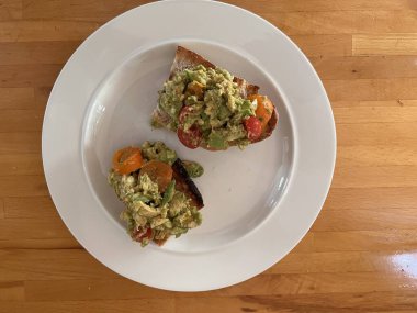Avokado meyvesiyle ezilmiş limon suyu ve ekşi hamurlu tost üzerine domates ve haşlanmış yumurta ve domatesleri kahvaltıda beyaz tabakta ya da öğle yemeği aperatifi ahşap arka plan düz görünüm.