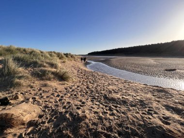 Holkham 'da deniz tuzlu suyla dolu güzel bir sahil manzarası çimenli kumlar arasında soğuk, sakin bir kış günü Norfolk Doğu Anglia' da mavi gökyüzü ve tatil yürüyüşü.