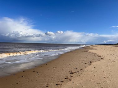 Kum tepecikleri ve alçak deniz gelgiti olan güzel kumlu sahil doğal manzarası mavi gökyüzünün altında tuzlu su ve Winterton Norfolk Doğu Anglia İngiltere 'de ilkbaharda bulut.  