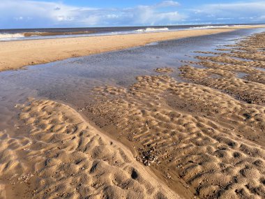 Kum tepecikleri ve alçak deniz gelgiti olan güzel kumlu sahil doğal manzarası mavi gökyüzünün altında tuzlu su ve Winterton Norfolk Doğu Anglia İngiltere 'de ilkbaharda bulut.  