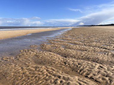 Kum tepecikleri ve alçak deniz gelgiti olan güzel kumlu sahil doğal manzarası mavi gökyüzünün altında tuzlu su ve Winterton Norfolk Doğu Anglia İngiltere 'de ilkbaharda bulut.  
