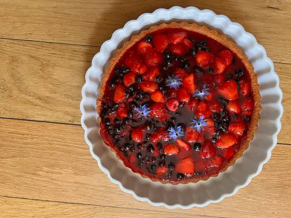 stock image Close up of freshly home baked healthy fruit flan of raspberries, strawberries, black and red currants from organic allotment organic garden on sponge base in white interior fluted tart dish flat lay