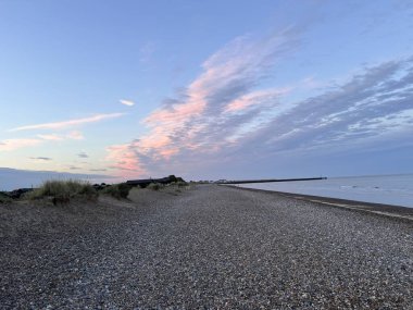 Güzel kumlu sahil manzarası, kumsalda kumsalda deniz suyu havuzları alçak okyanus gelgitleri ve gün batımında açık mavi gökyüzü. Norfolk 'ta kışın arka planda çimenli tepe kayalıkları ile gün batımına bakıyor.