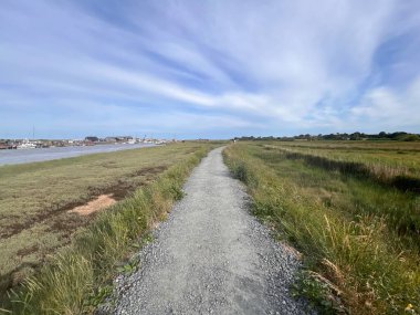 Suffolk sahilinin güzel manzarası Walberswicj Southwold yakınlarındaki yolda yürüyor, hiç insan yok, nehir kenarında yeşil çimenler ve mavi gökyüzü ve gün ışığında açık beyaz bulutlar