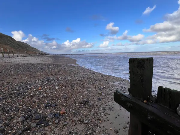 Fırtınalı bir günde kumlu kumlu bir sahil manzarası ahşap iskele Groyne yapısı okyanus ufkuna bakan büyük dalgalar ve Doğu Anglia 'da kışın mavi gri dramatik bulutlar. 