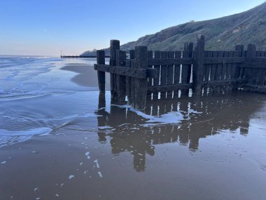 Güzel kumlu sahilde eski ahşap iskele alçak gelgitte deniz kenarına bakan soğuk kış günü Trimmingham Norfolk Doğu Anglia 'da mavi gökyüzünü ve okyanusu yansıtan su havuzları.