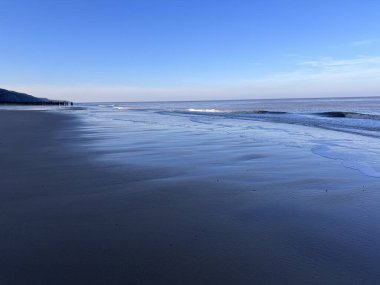 Beautiful beach landscape in Winter at sun down with blue clear sky and wood groyne sea defence looking out to ocean with skies and cloud  reflected in salt water pool on sany shore with pebbles clipart