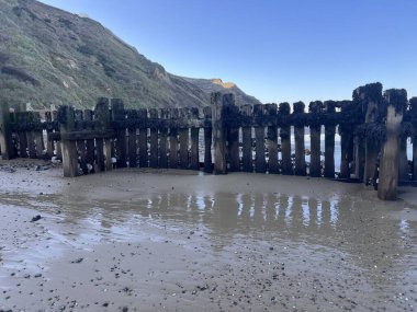 Old wooden jetty pier on the beautiful sandy beach at low tide looking out to sea at sundown pools of water reflecting blue skies and ocean on cold Winter day in Trimmingham Norfolk East Anglia uk clipart