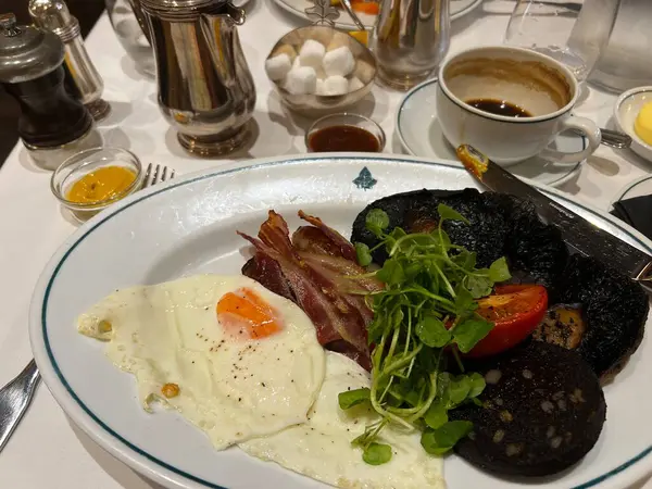İngiliz kahvaltısı, kızarmış yumurta, pastırma, siyah puding, sosis, domates mantarı, fincan kahve. Ve gümüş kaplar ve tereyağlı çatal bıçak seti otel restoranında beyaz keten masa örtüsünün üzerinde.