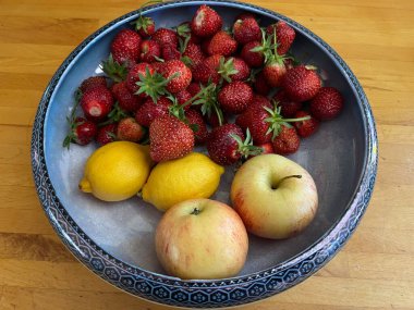 Bir kase çilek, limon ve elma, olgun meyve suyu meyvesi taze organik çiftlik bahçesi tahsisi ve meyve bahçesi yaz aylarında ahşap mutfak arka planında antik seramik kasede.