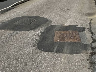 Tamamlanmamış yolun kapanışı sert gri asfalt yüzeyi çakıl taşı çatlakları ve metal drenaj kapağı ile işliyor. Yoldan çıkan çıkıntılar ve hanedanlığın kaldırımları düz değil. Beyaz çizgili işaretleri olan kimse yok.