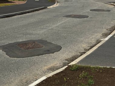 Tamamlanmamış yolun kapanışı sert gri asfalt yüzeyi çakıl taşı çatlakları ve metal drenaj kapağı ile işliyor. Yoldan çıkan çıkıntılar ve hanedanlığın kaldırımları düz değil. Beyaz çizgili işaretleri olan kimse yok.