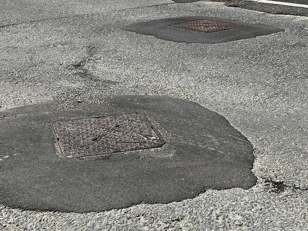 Tamamlanmamış yolun kapanışı sert gri asfalt yüzeyi çakıl taşı çatlakları ve metal drenaj kapağı ile işliyor. Yoldan çıkan çıkıntılar ve hanedanlığın kaldırımları düz değil. Beyaz çizgili işaretleri olan kimse yok.