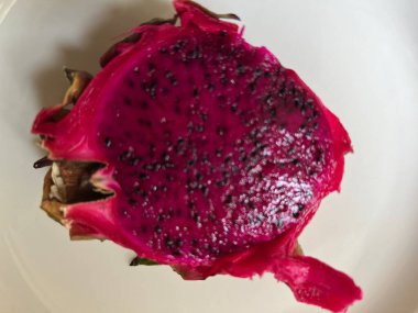 Ejderha meyvesi Pitahaya 'ya yaklaş lezzetli, yenilebilir, sulu, sağlıklı, siyah tohumlu kırmızı meyve ve yapraklı, beyaz porselen tabağın üst görüntüsü. 