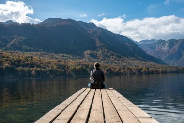 Küçük bir iskelede oturuyor ve Triglav Ulusal Parkı 'ndaki Bohinj Gölü manzarasının tadını çıkarıyor. Julian Alpleri, Slovenya